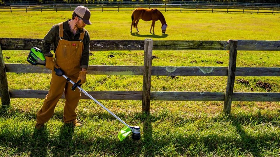 A man in overalls holding a trimmer and a horse in the background
