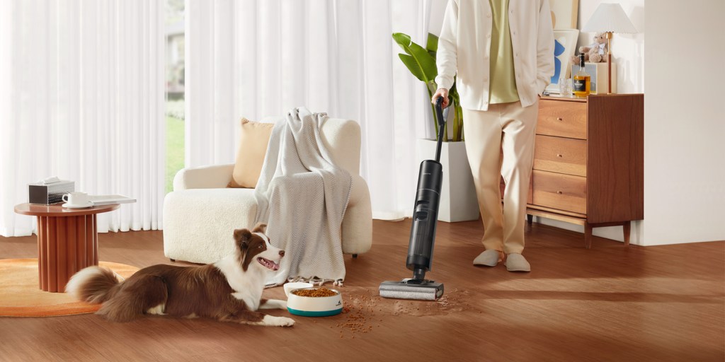 A person with a vacuum cleaner and a dog lying on the floor
