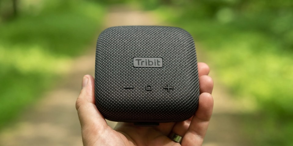 A hand holding a black square speaker