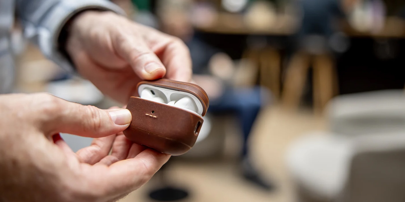 A person holding a brown case with white earbuds