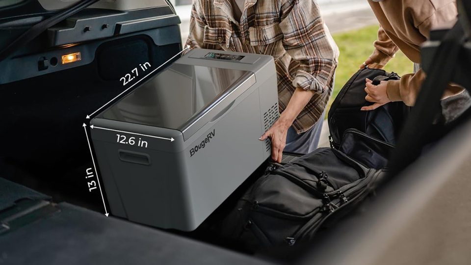 A person putting a large grey box into a luggage