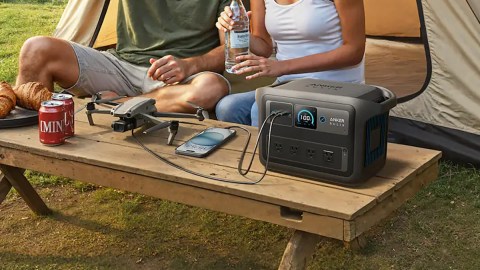 A man and woman sitting on a table with a drone and a bottle of water
