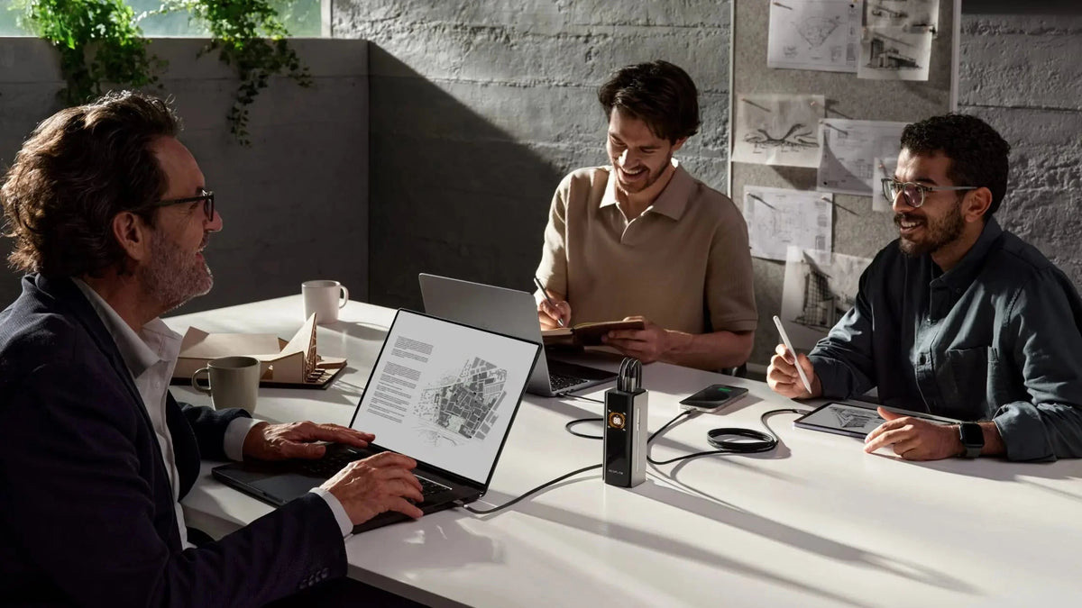 A group of people sitting at a table with laptops and a pen
