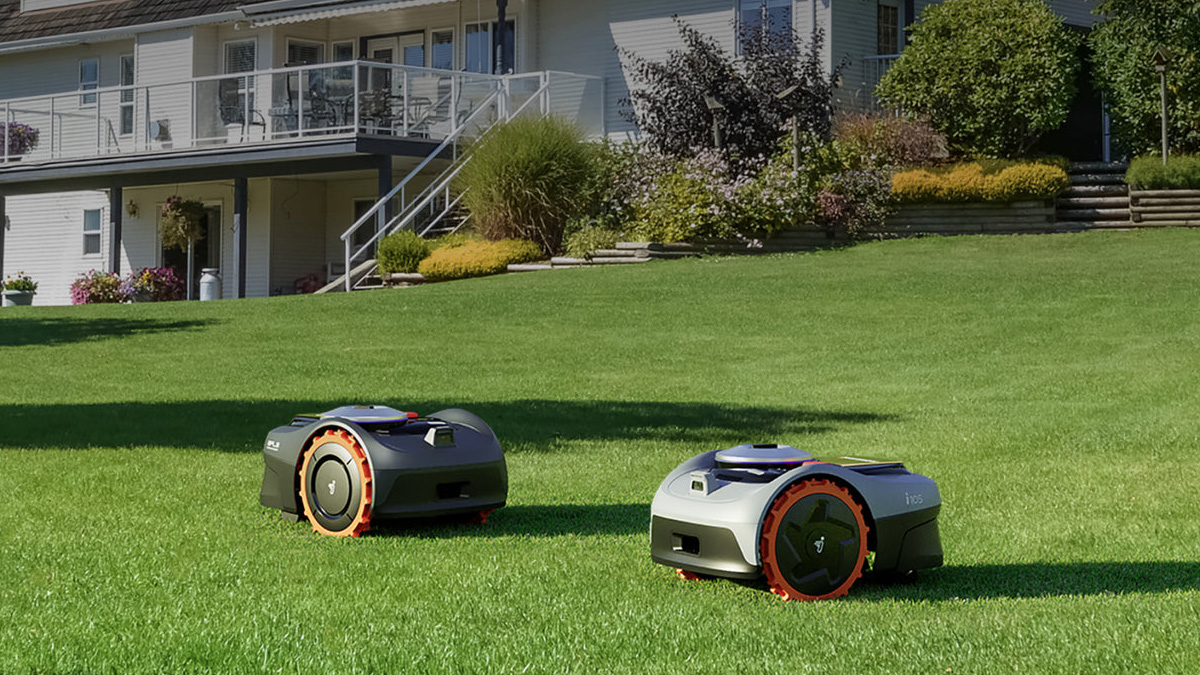 Two robotic lawnmowers on grass in front of a house