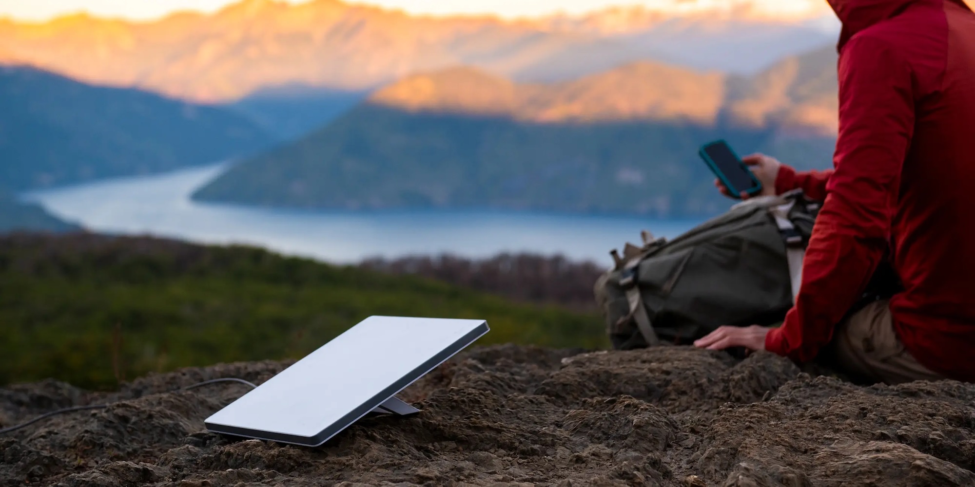 A person sitting on a rock with a tablet in front of mountains