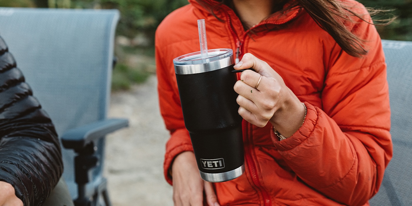A person holding a black and silver cup with a straw