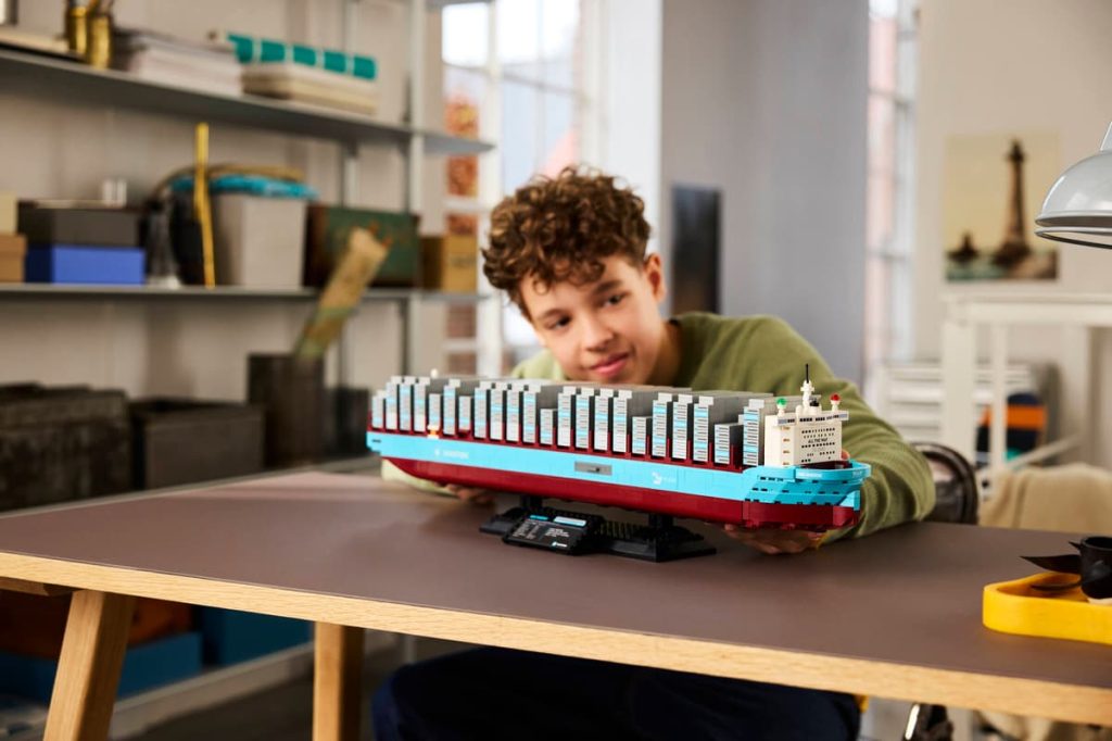 A boy sitting at a table with a LEGO Maersk ship