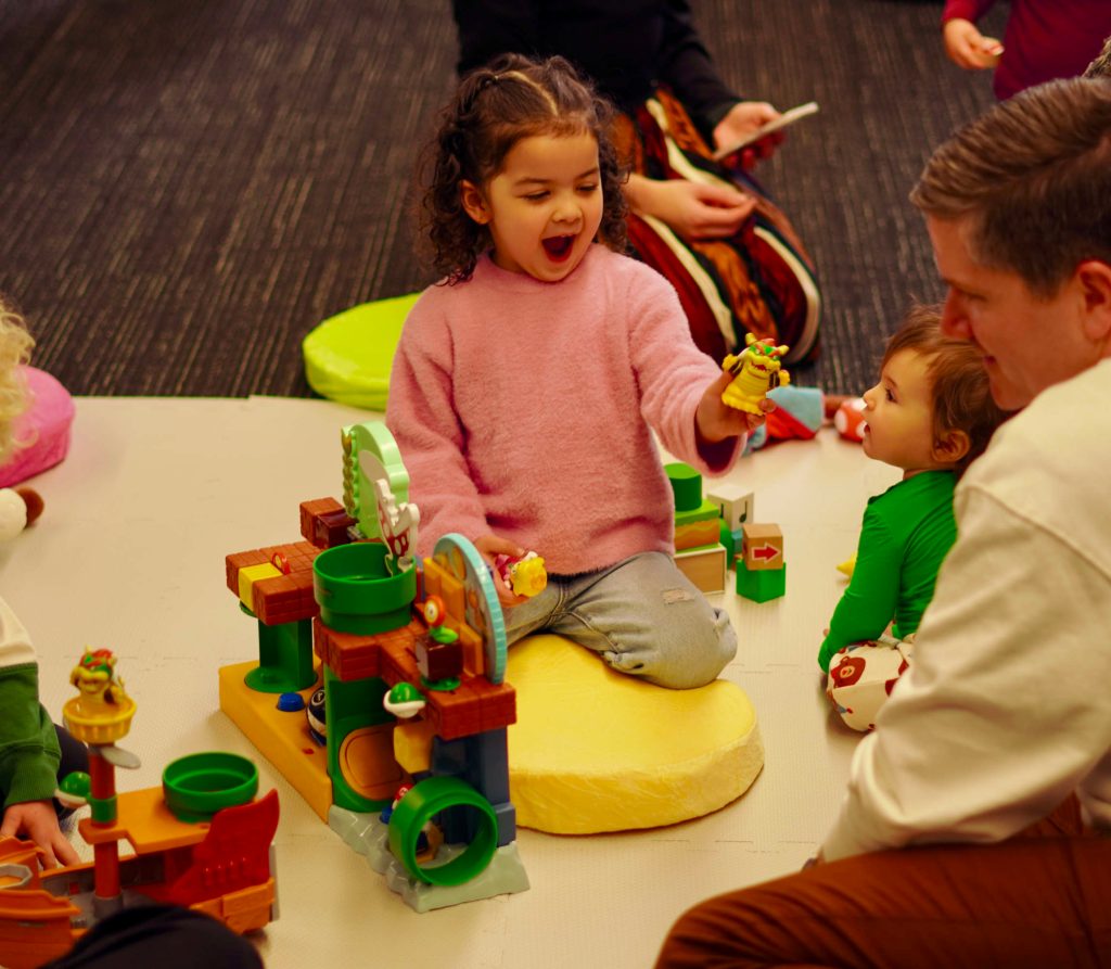 A group of people sitting on the floor with a girl playing with toys