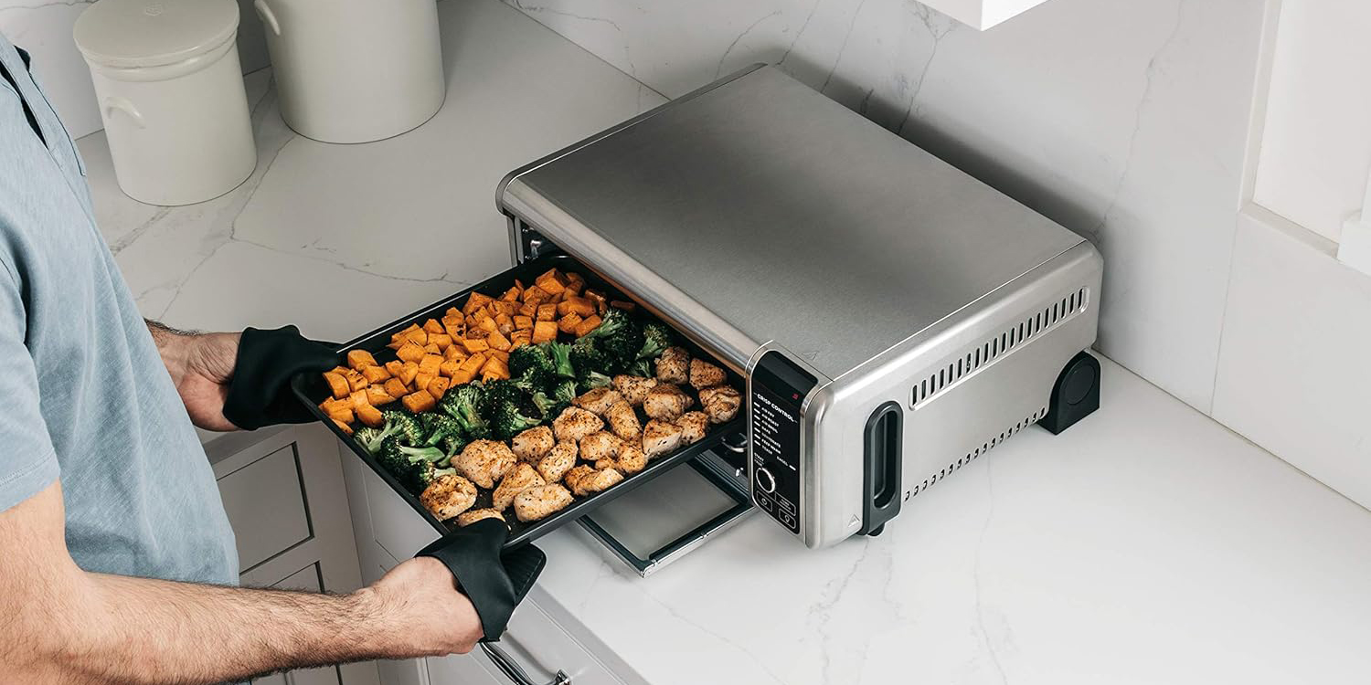 A person holding a tray of food in a toaster oven