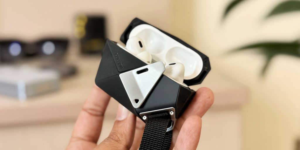 A hand holding a black and white case with white and silver earbuds