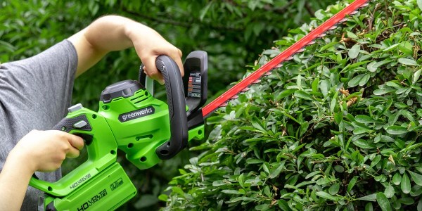 A person holding a green and black electric hedge trimmer