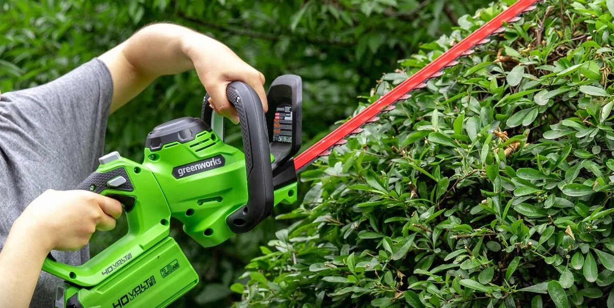 A person holding a green and black electric hedge trimmer