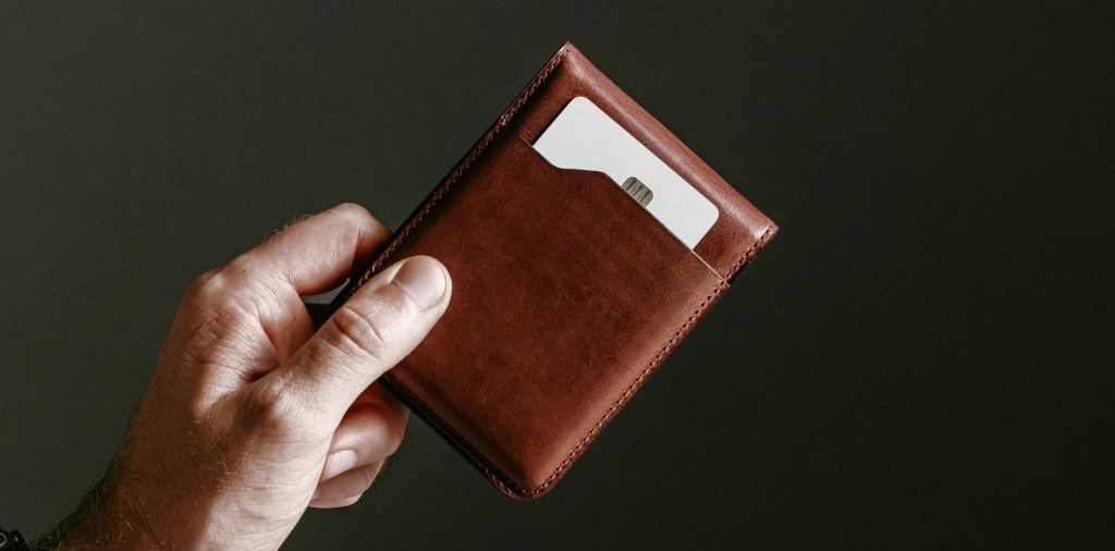 A hand holding a brown leather wallet
