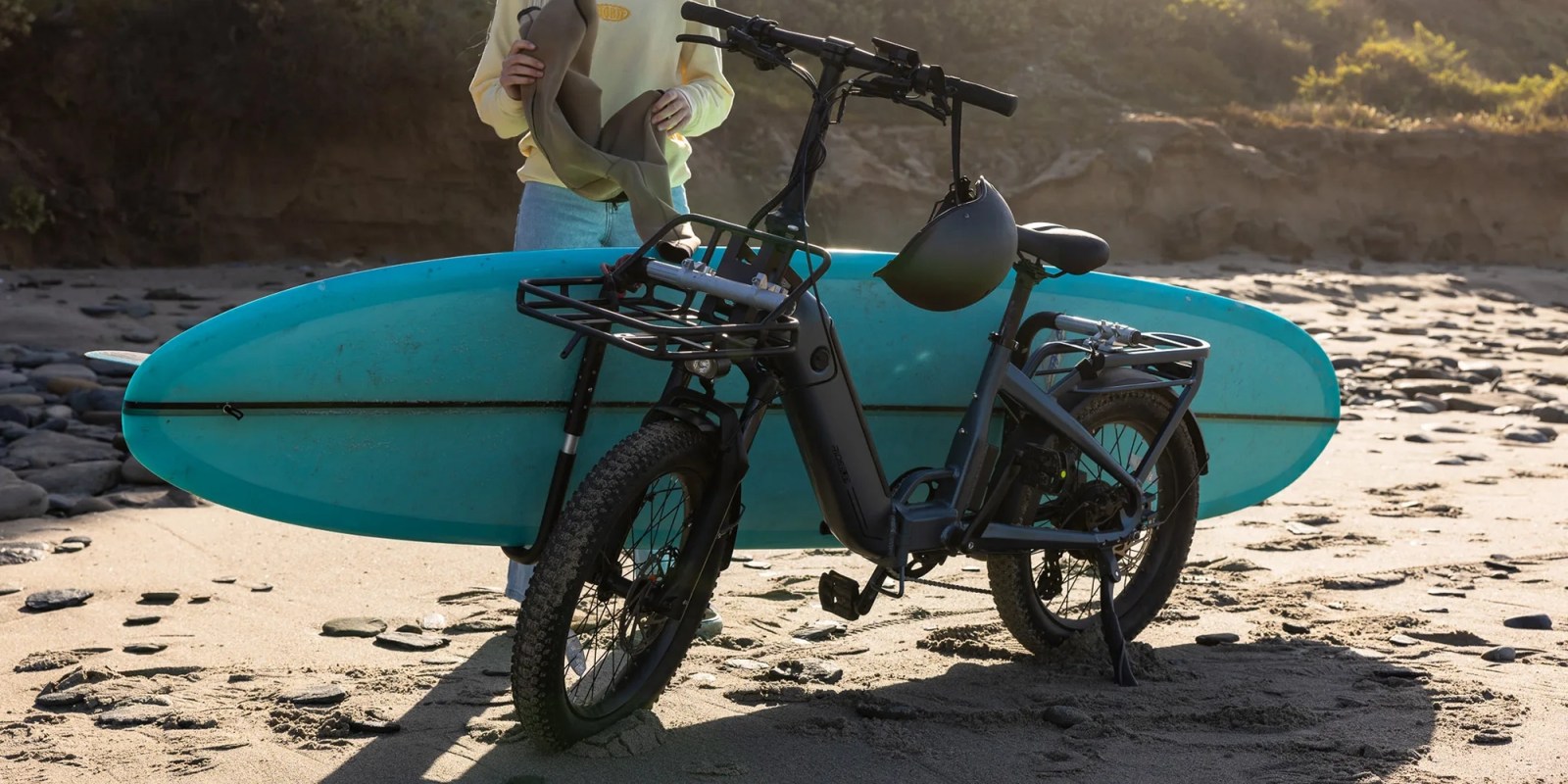 A person holding a surfboard next to a bicycle