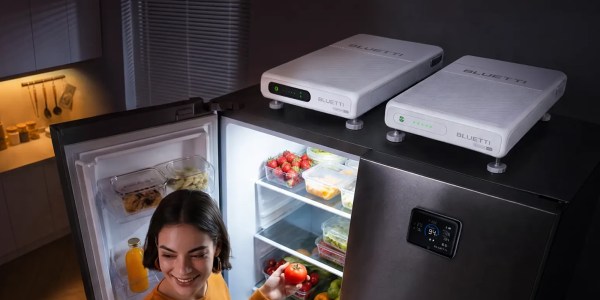 A woman looking at a tomato in front of a refrigerator