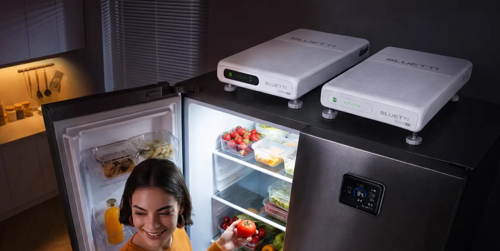A woman looking at a tomato in front of a refrigerator