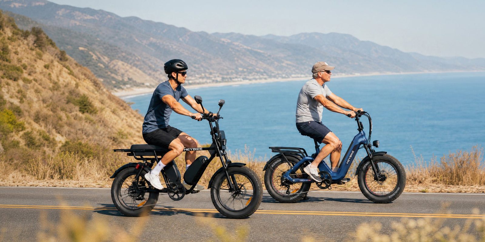 Two men riding electric bikes on a road with water in the background