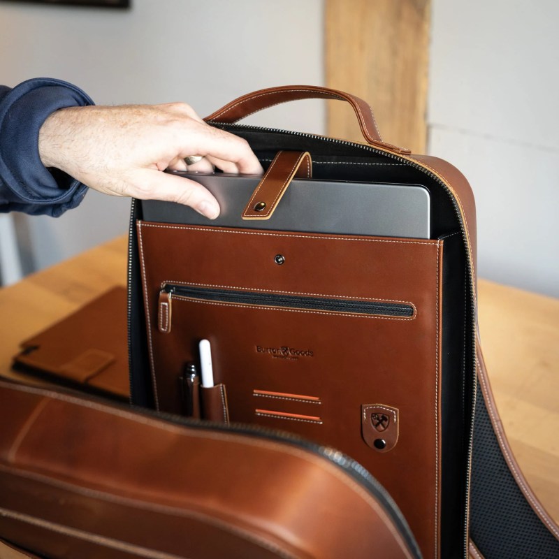 A hand holding a laptop in a brown leather bag