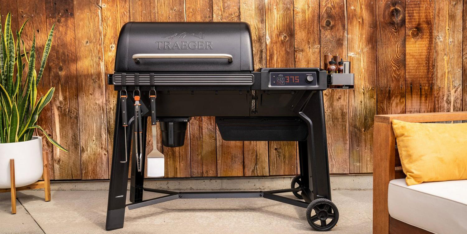 A black barbecue grill with a wood wall behind it