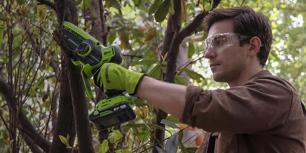 A man wearing goggles and gloves holding a green and black cordless saw